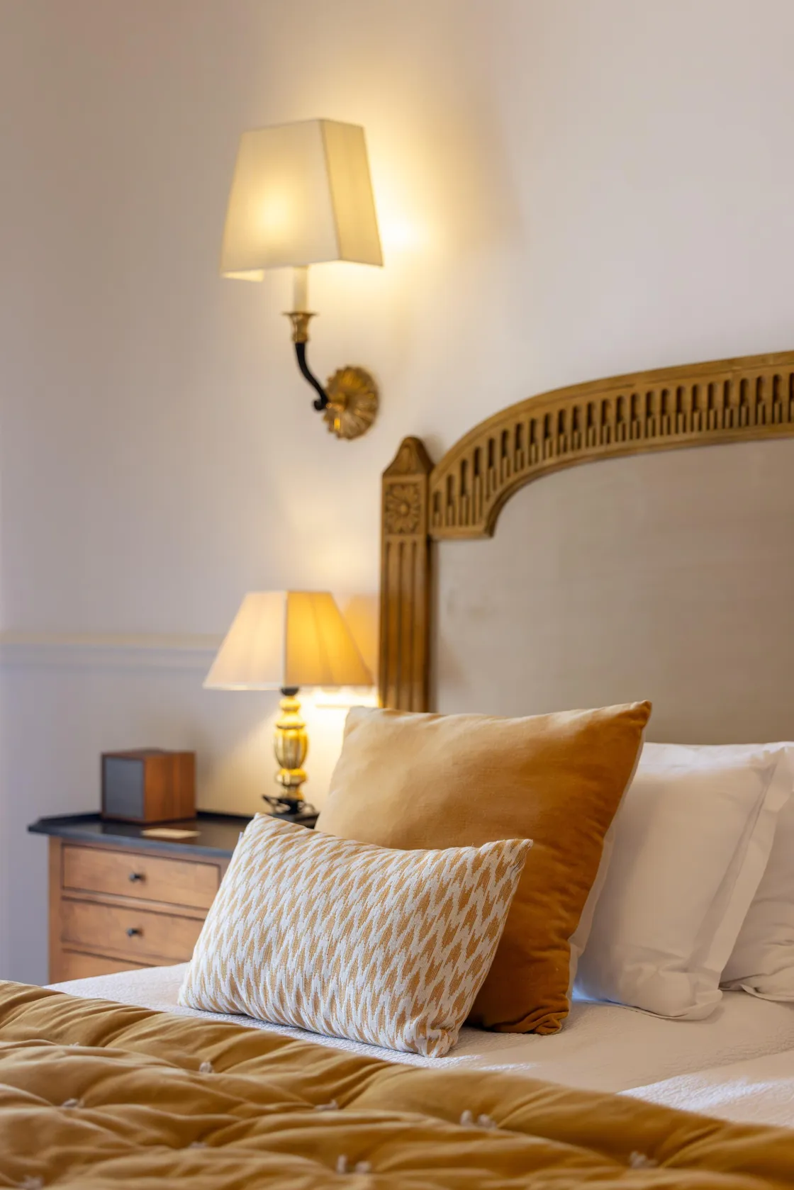 Lit avec une tête de lit en bois orné, des coussins et une lampe de chevet allumée
