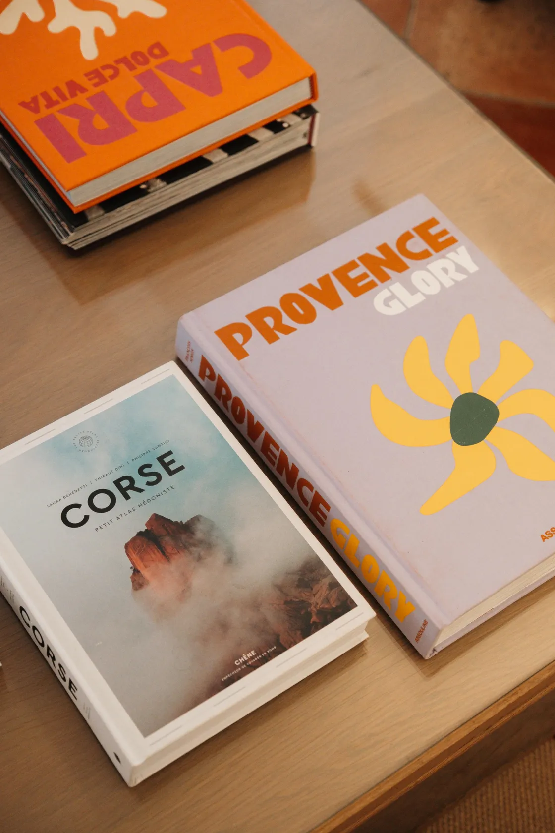 Trois livres posés sur une surface en bois, dont un intitulé "Corse" et un autre "Provence Glory"