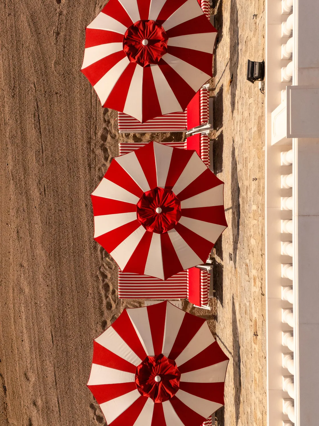 Quatre parasols rayés rouges et blancs alignés sur une plage de sable