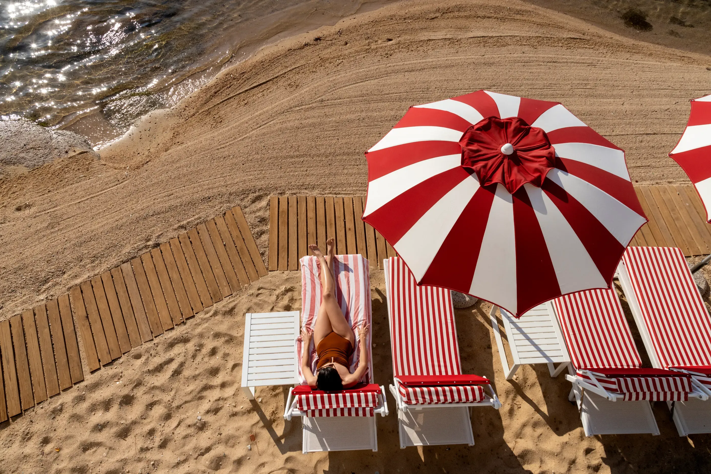 Une personne allongée sur un transat à côté de la mer, sous un parasol rayé rouge et blanc