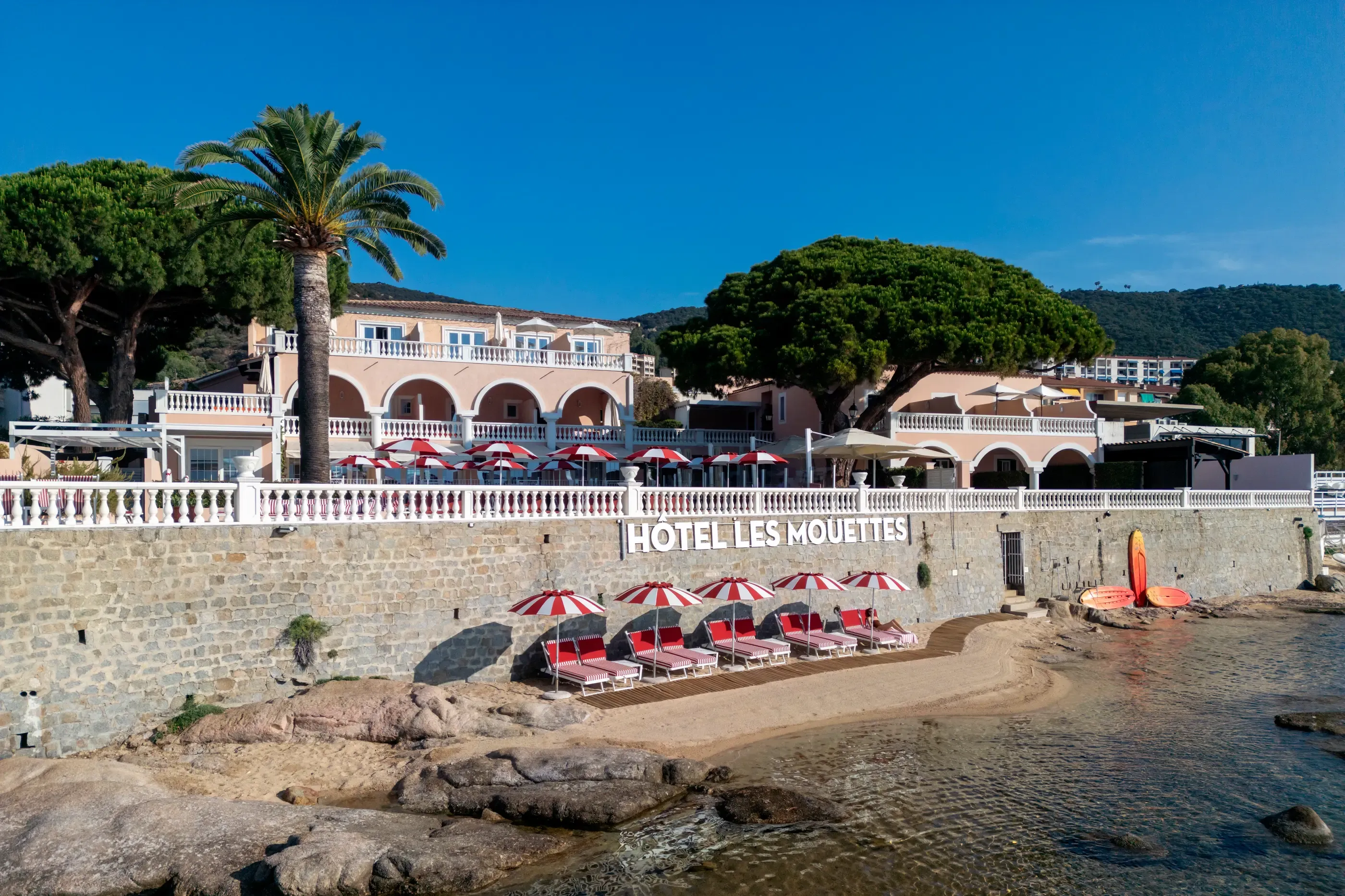 Hôtel Les Mouettes avec une terrasse et des chaises longues en bord de mer sous des parasols rouges et blancs